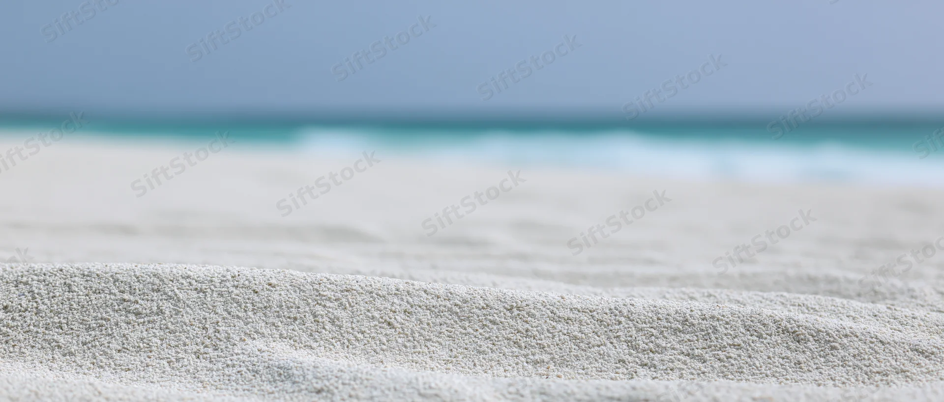Close-up of white sandy beach with rippled texture and ocean in the distance