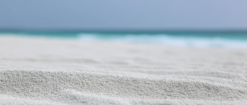 Close-up of white sandy beach with rippled texture and ocean in the distance