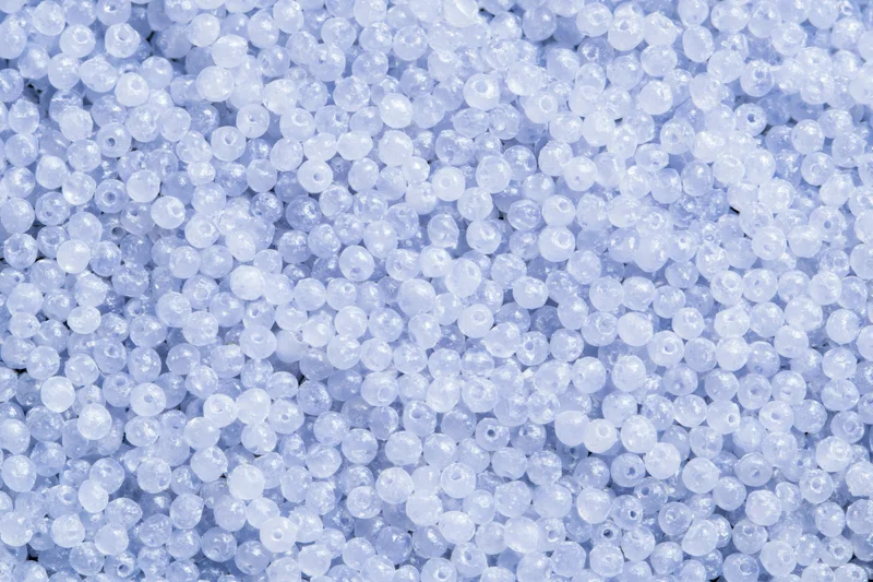Closeup of tiny translucent white and blue plastic beads densely packed in a uniform pattern