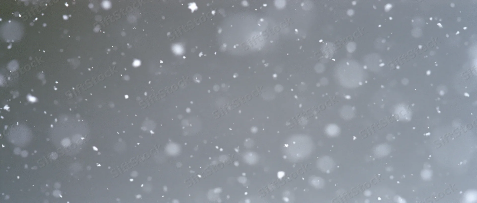 Snow particles falling midair against a grey background