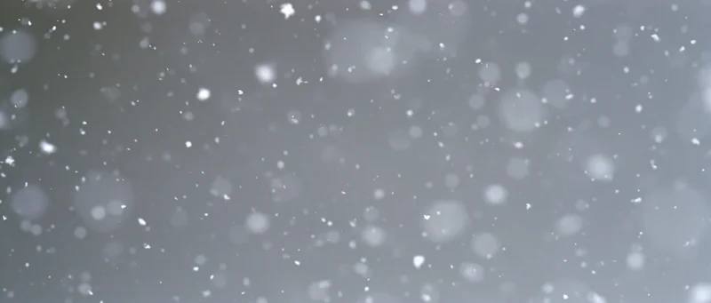 Snow particles falling midair against a grey background