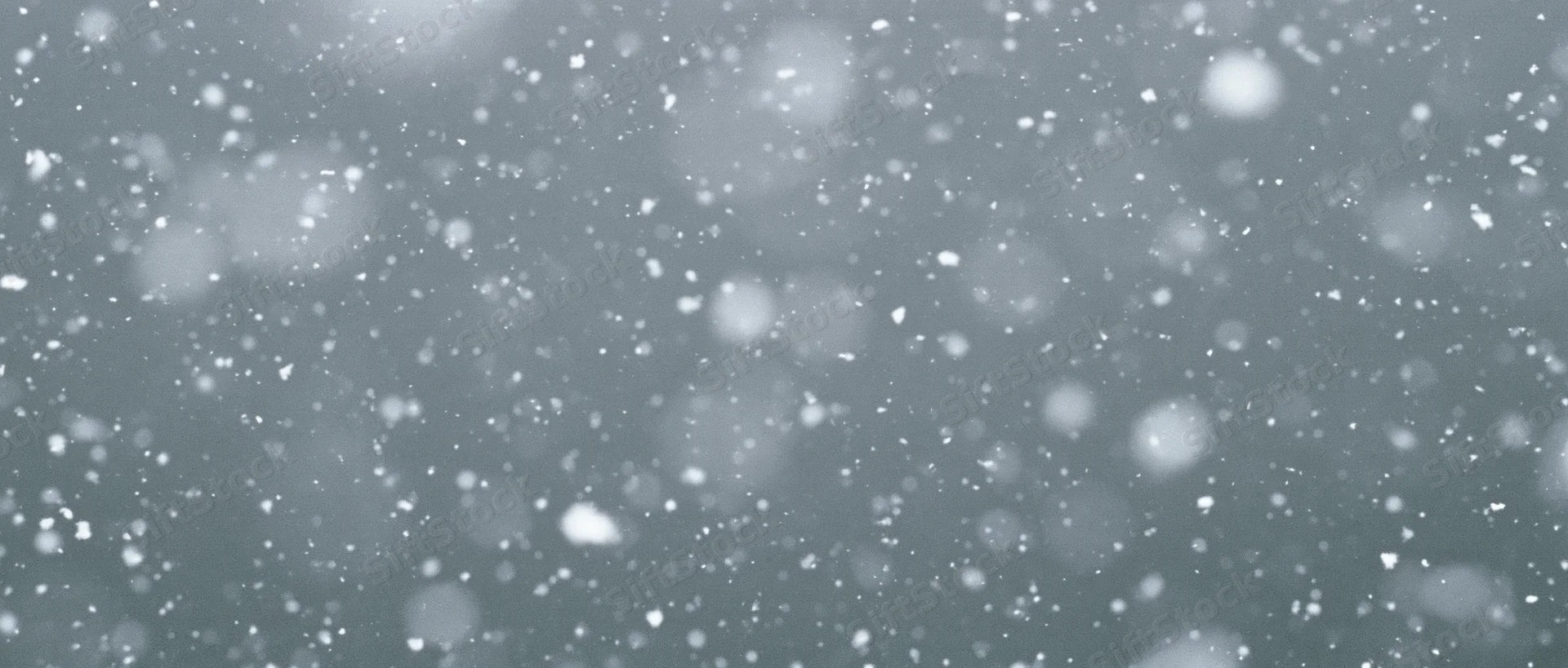 Snow particles falling midair against a grey background