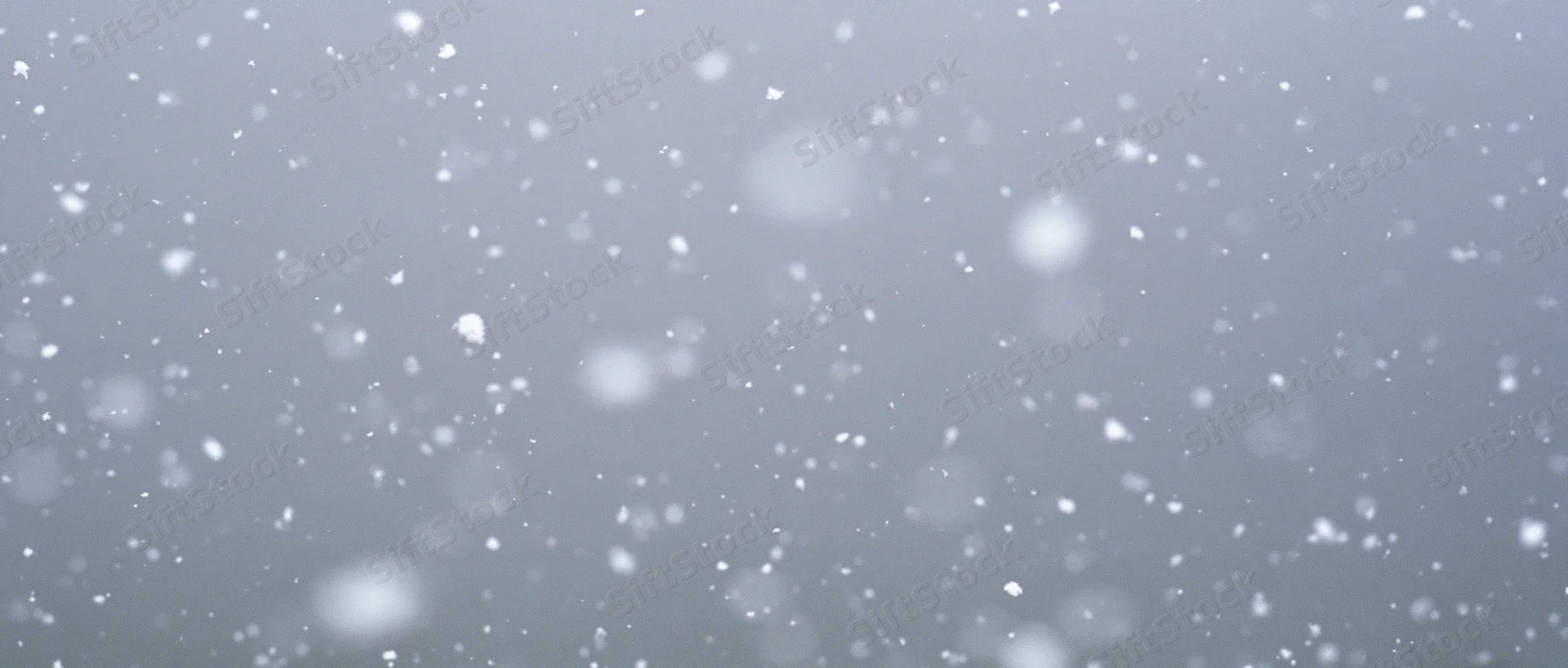 Snow particles falling mid-air against a grey sky background