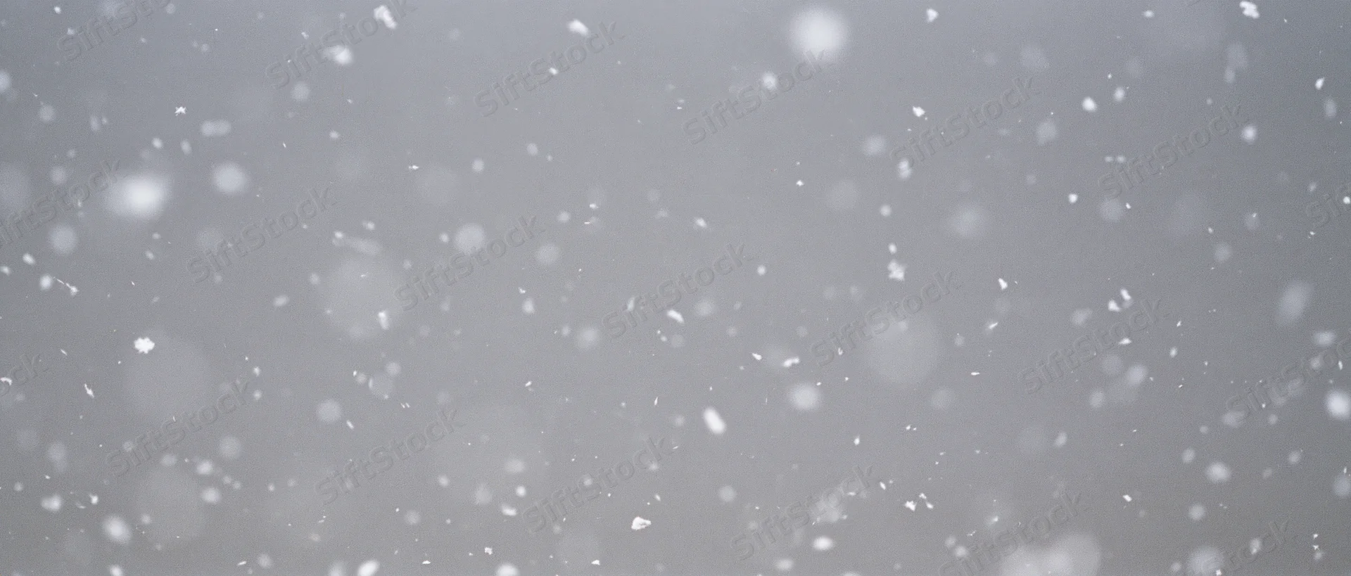 Snow particles falling midair against a grey background