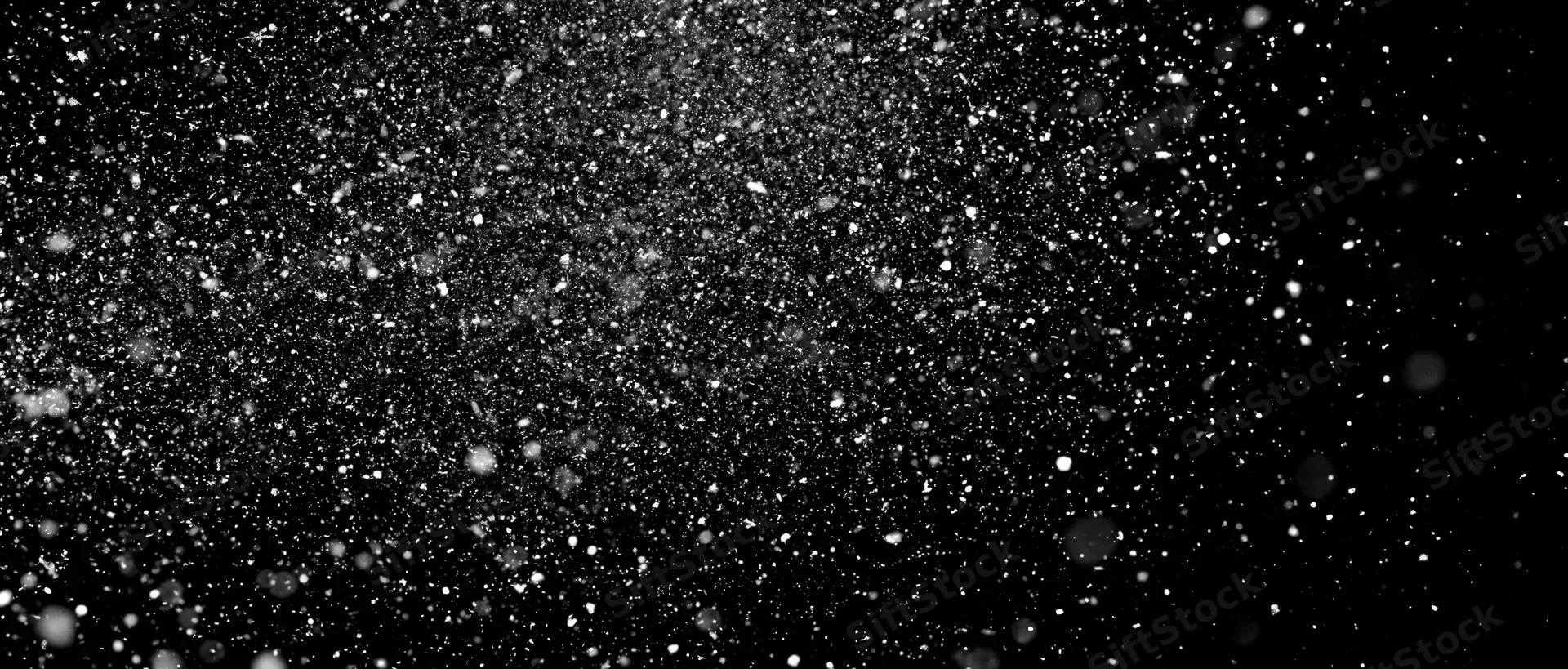 Snow particles falling midair against a black background