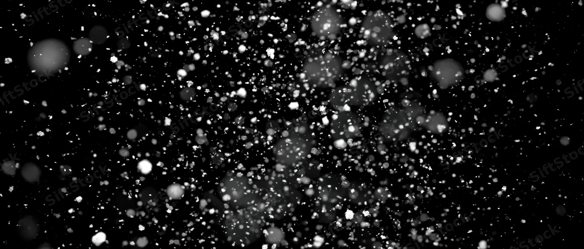Snow particles falling midair against black background