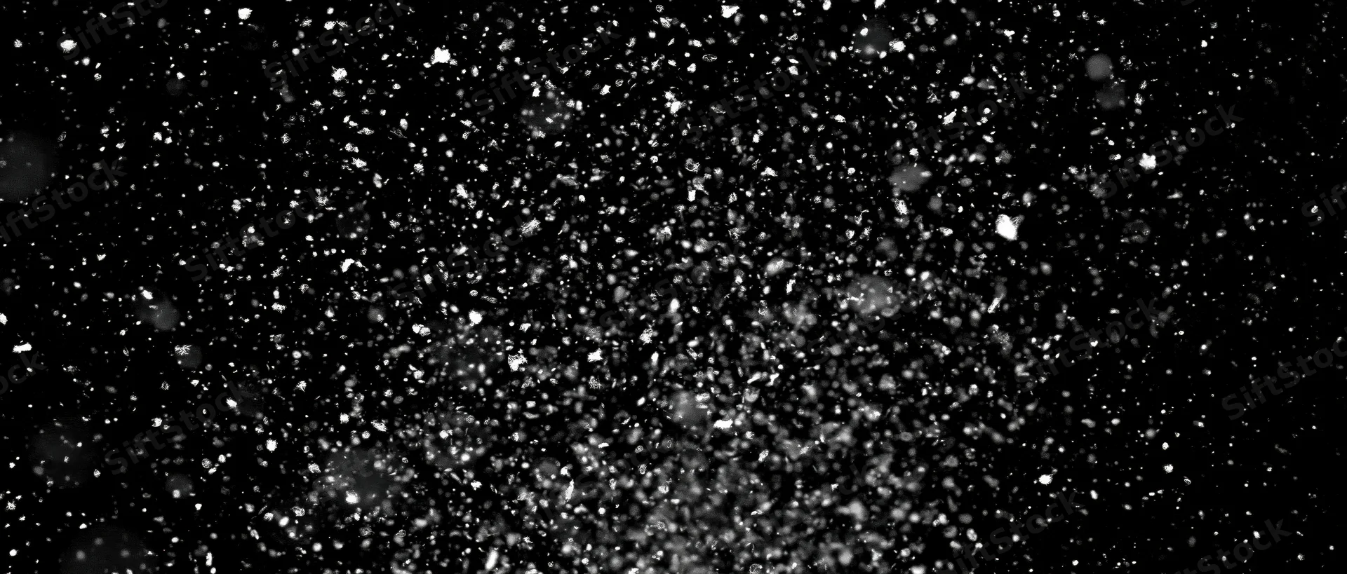 Snow particles falling midair against a black background