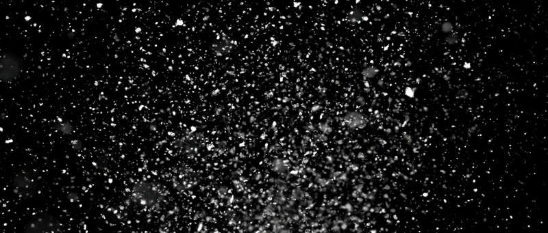 Snow particles falling midair against a black background