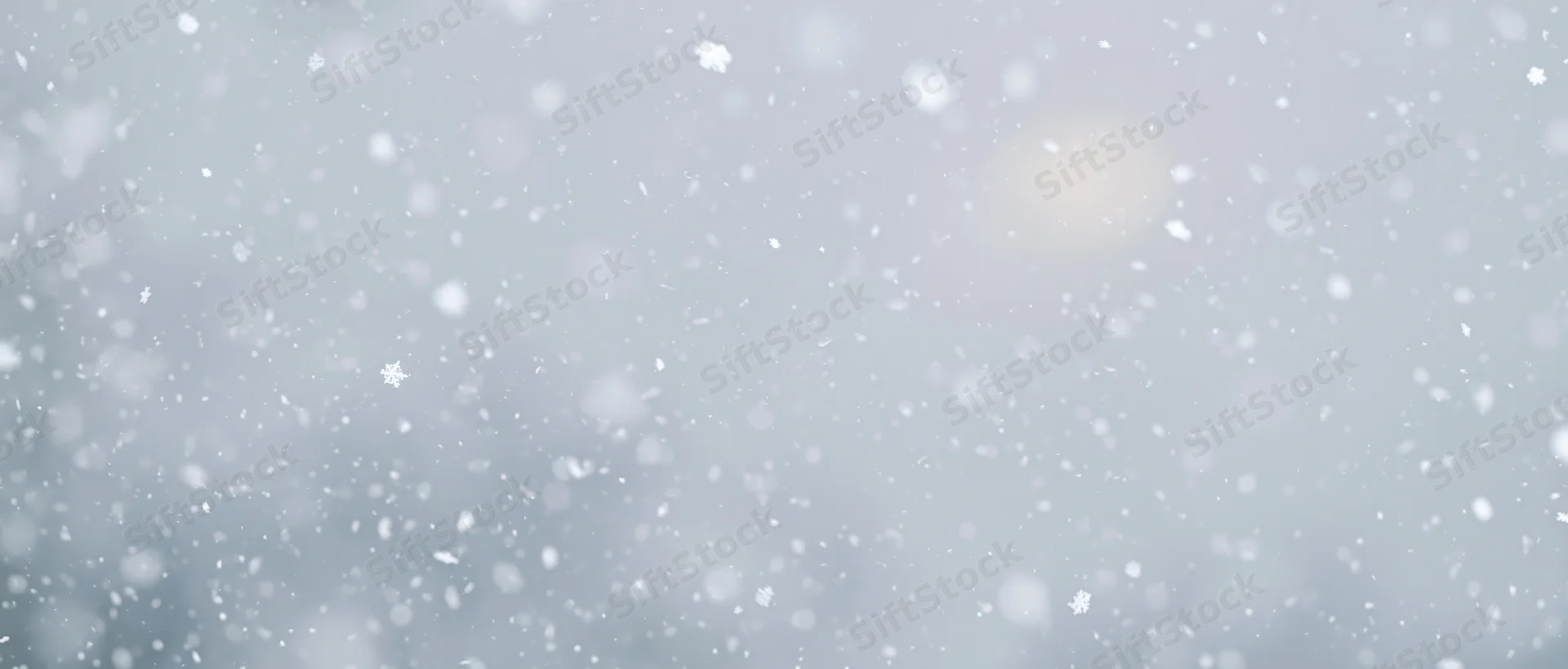 Snowflakes falling against a pale gray sky with soft bokeh and blurred background
