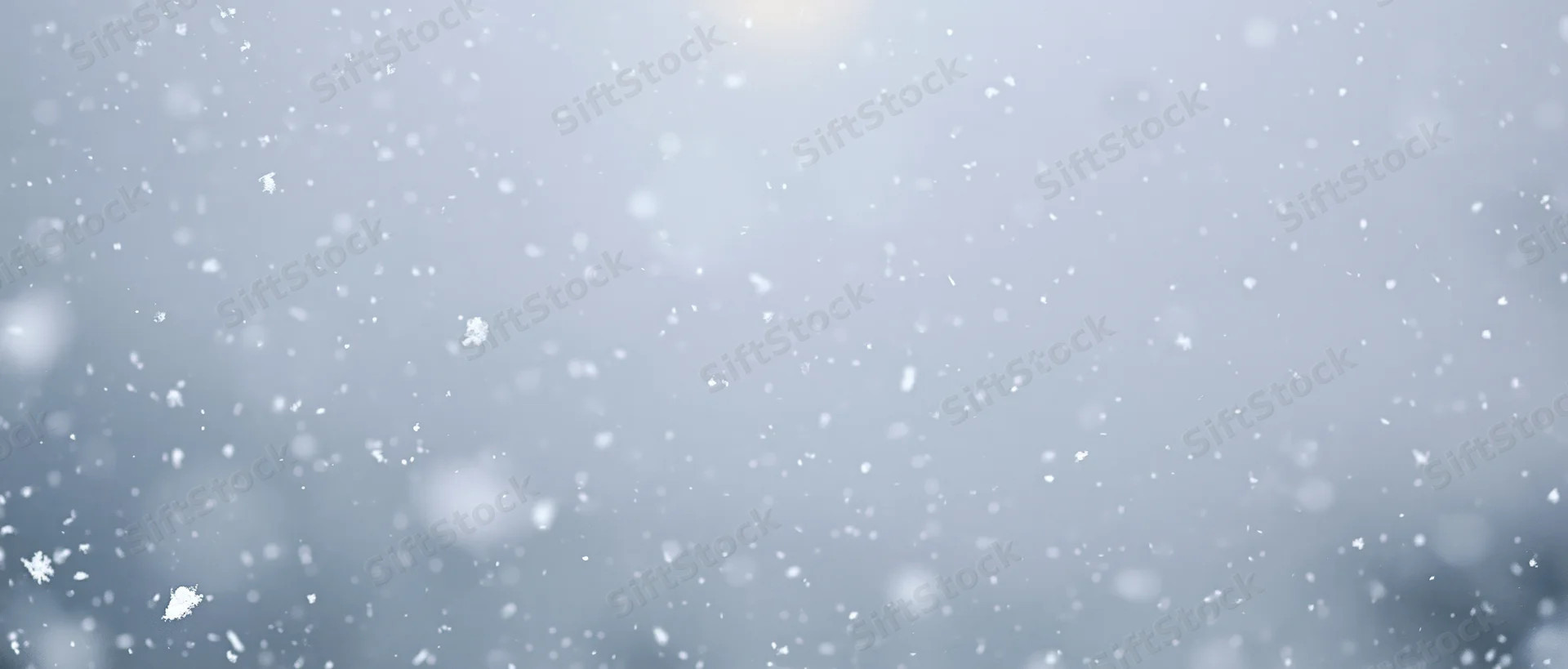 Snowflakes falling against a pale sky with soft bokeh background
