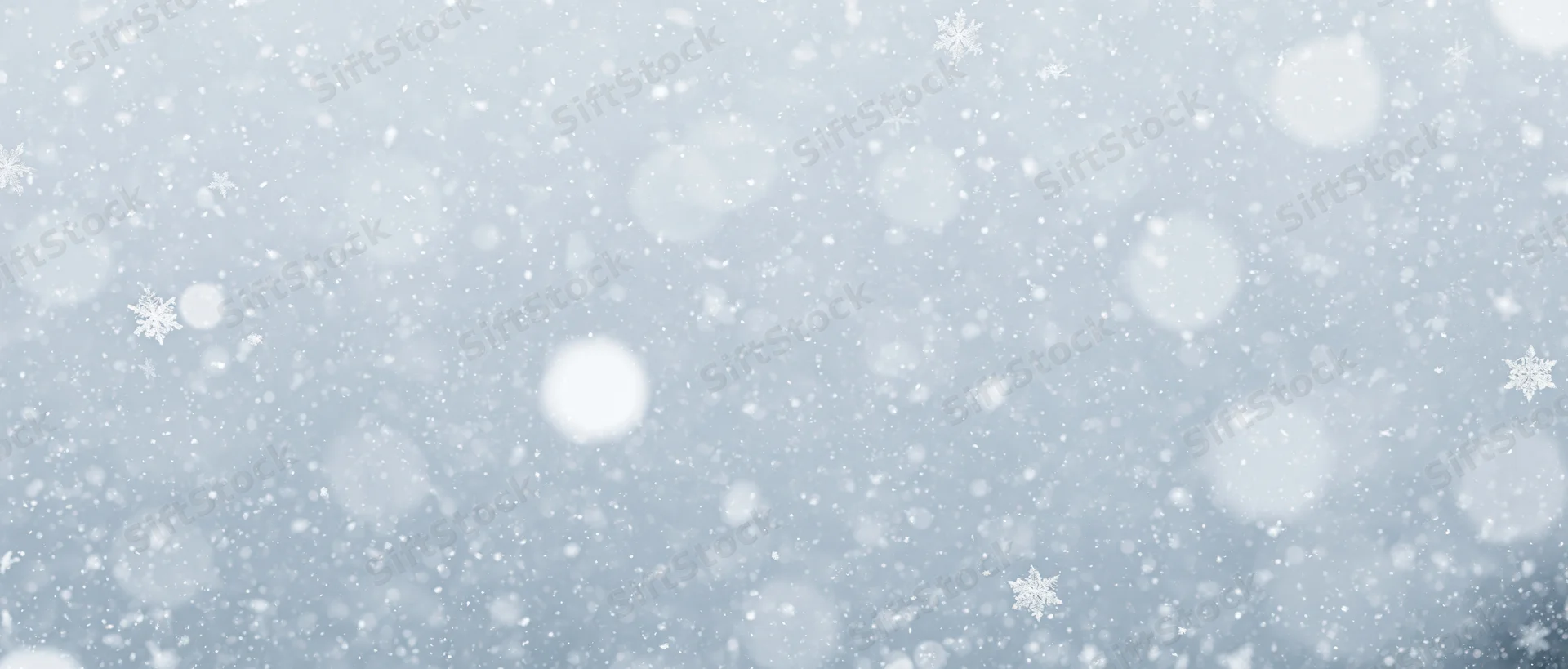 Falling snowflakes and soft bokeh particles scattered across a light blue winter sky