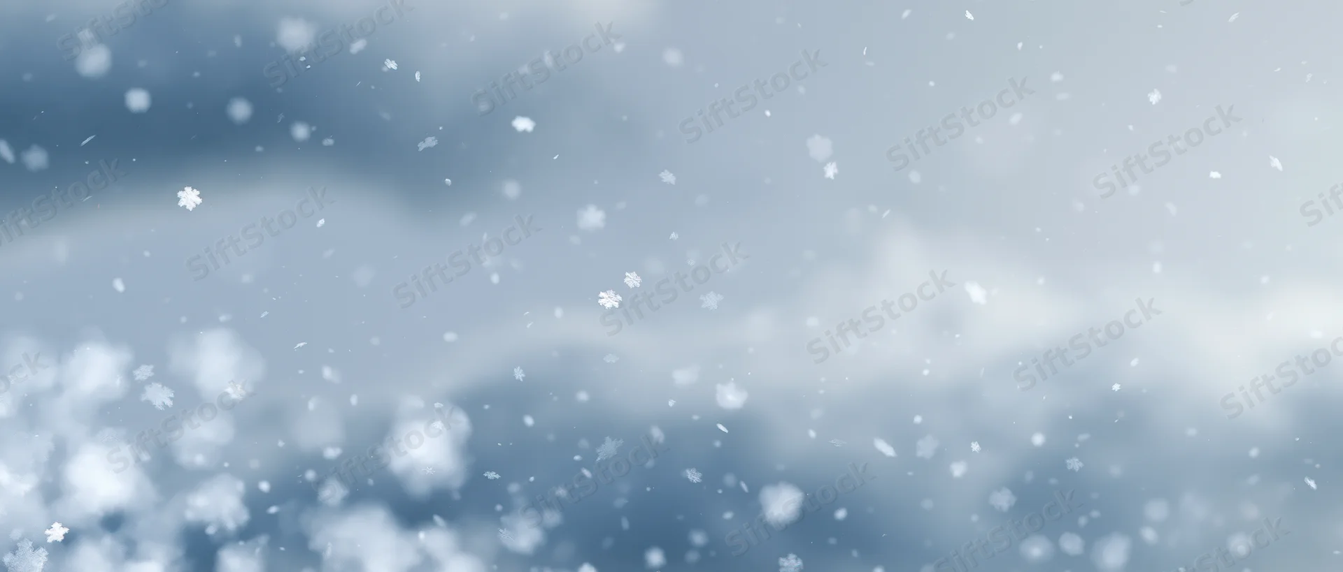 Snowflakes falling through a pale winter sky with soft clouds in the background