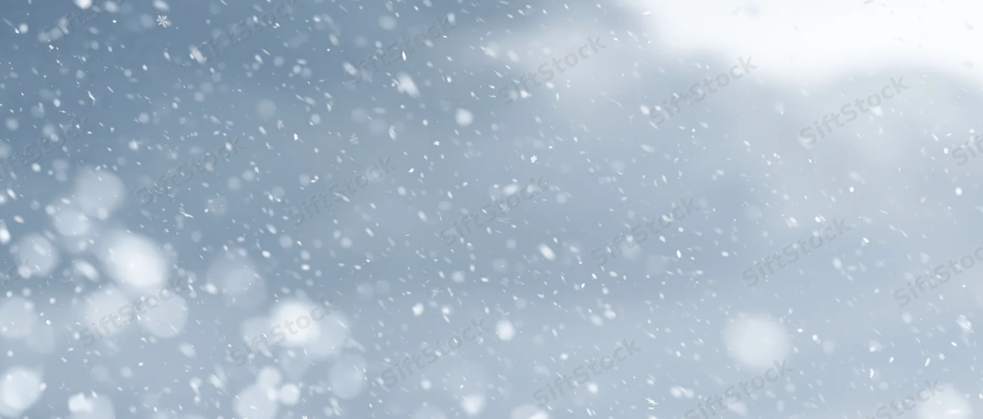 Snowflakes falling through a pale winter sky with soft bokeh and light clouds