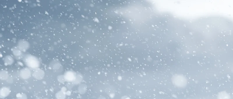 Snowflakes falling through a pale winter sky with soft bokeh and light clouds