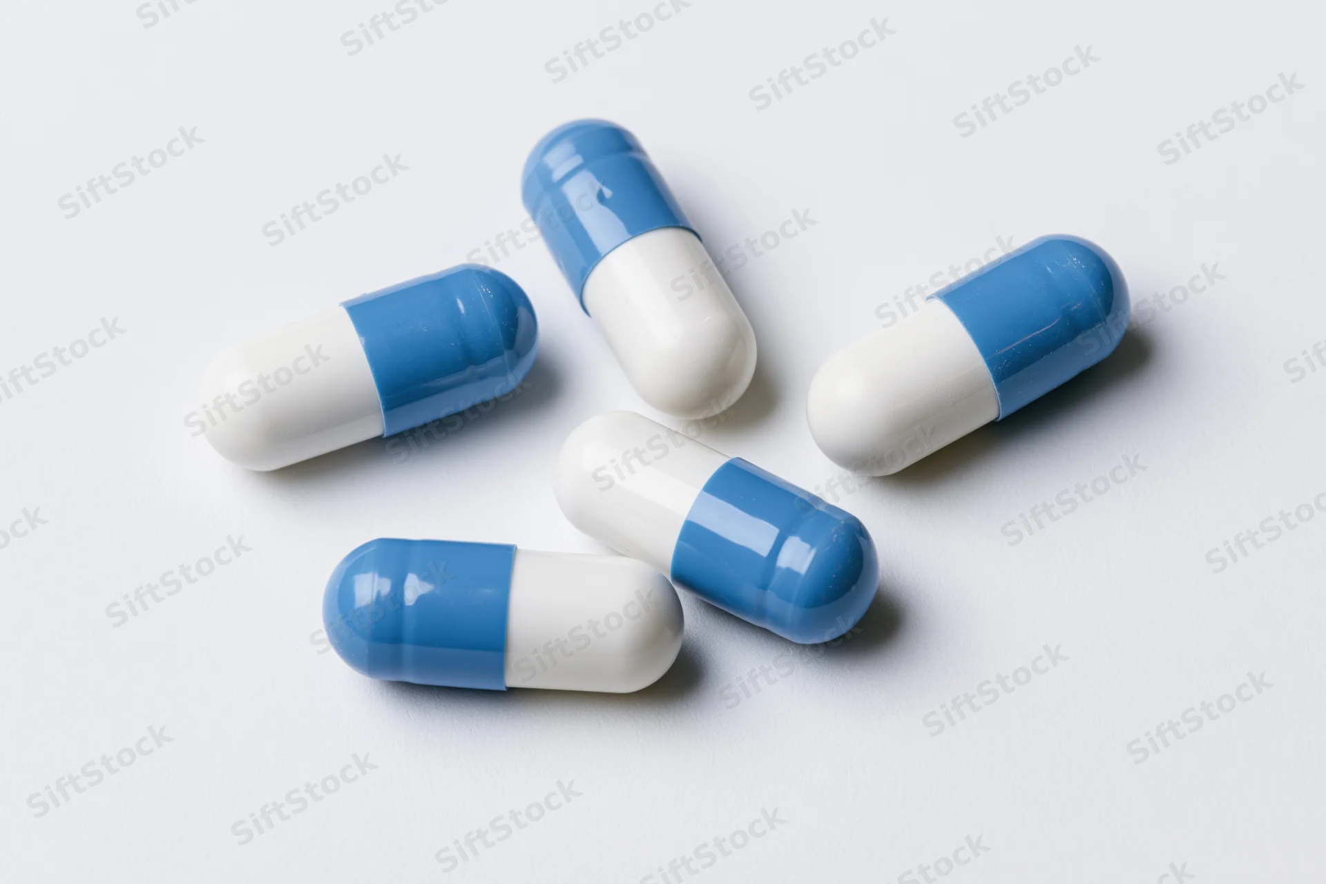 Five blue and white gelatin capsules scattered on a white surface