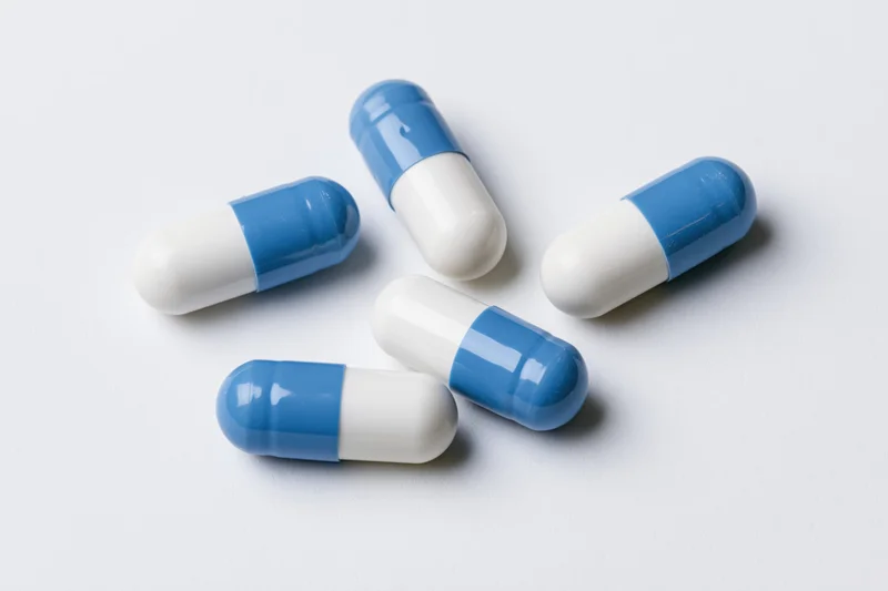 Five blue and white gelatin capsules scattered on a white surface
