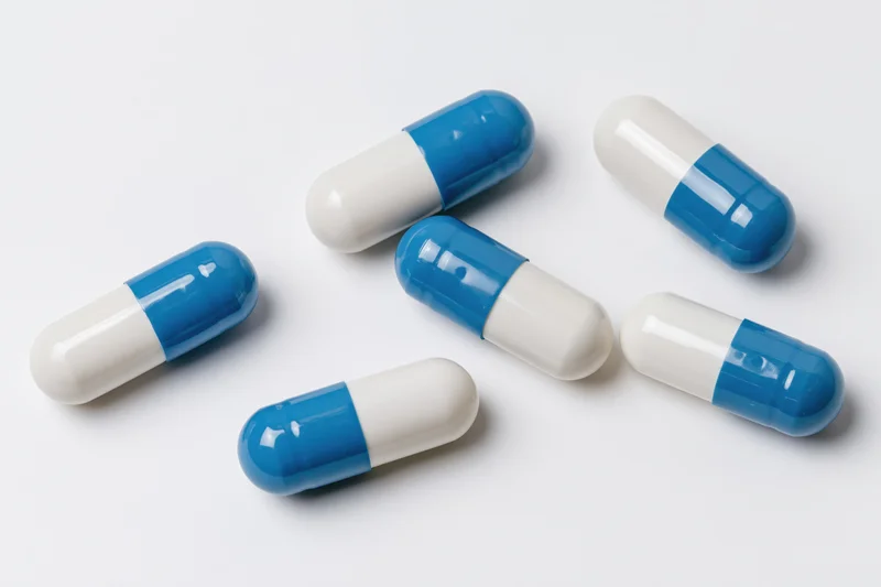 Blue and white gelatin capsules scattered on a white surface