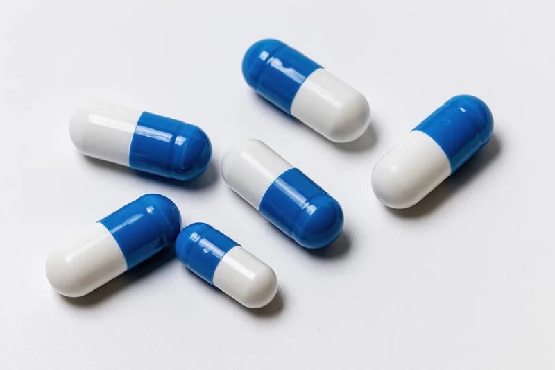 Blue and white gelatin capsules scattered on a white surface