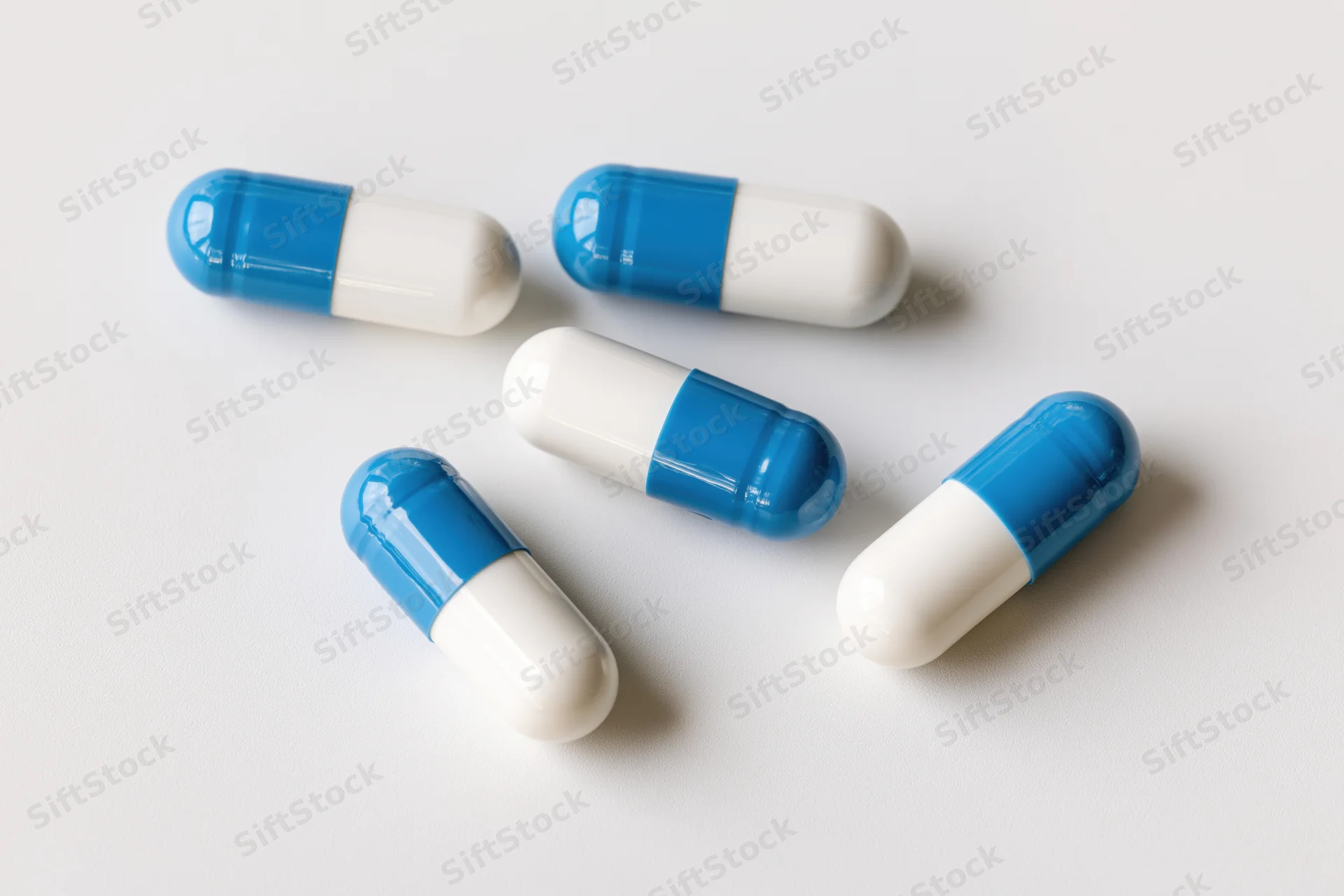 Five blue and white gelatin capsules scattered on a white surface
