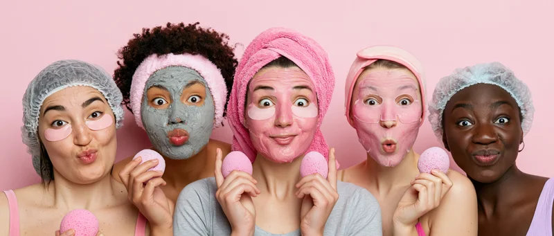 Five diverse young women in skincare routines with facial masks and sponges against pink background