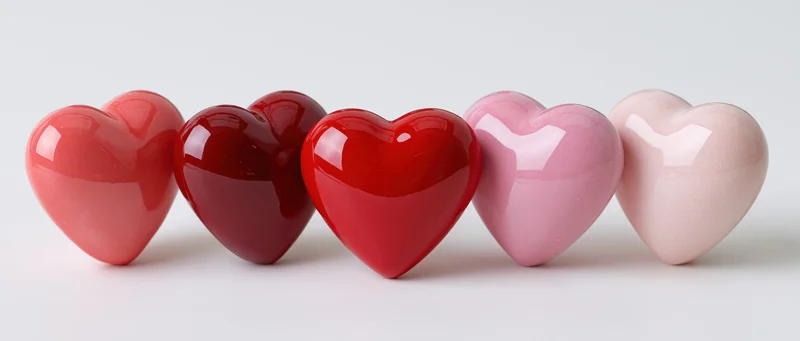 Five glossy heart-shaped decorative objects arranged in a row on a white surface