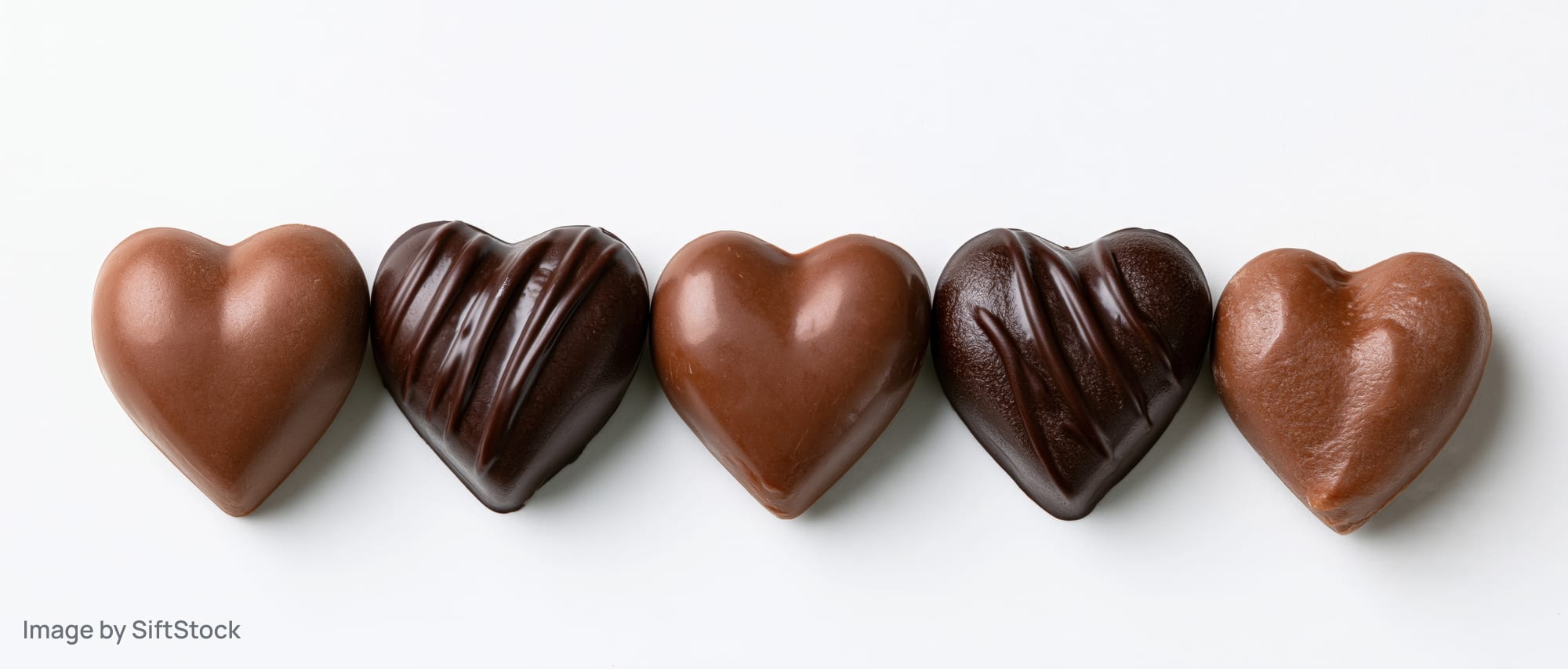 Five heart-shaped chocolate candies arranged in a row on a white background