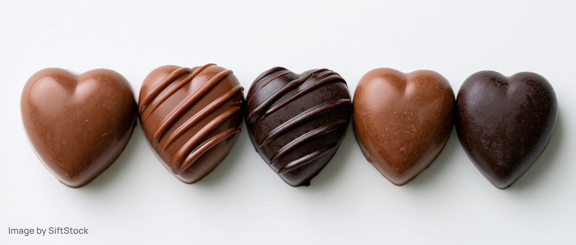 Five heart-shaped chocolate candies arranged in a row on a white surface