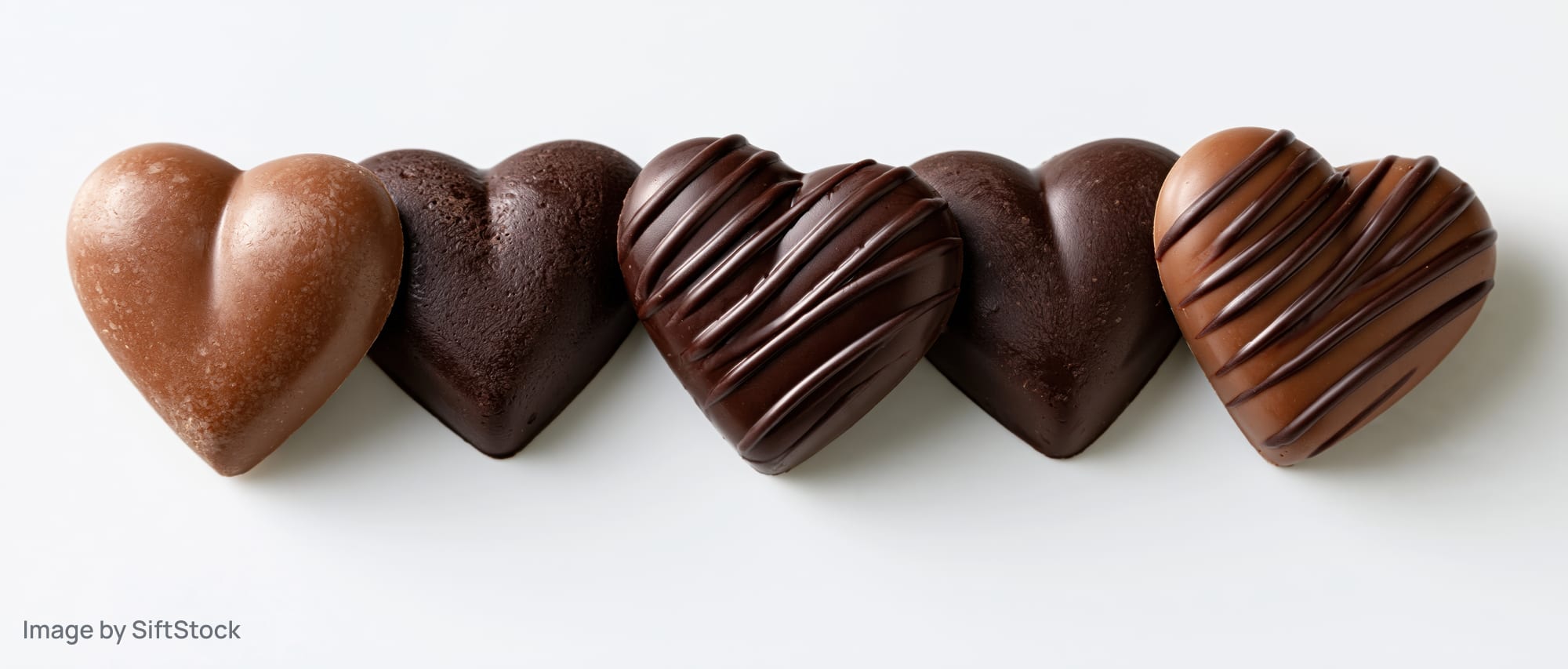 Five heart-shaped chocolate candies arranged in a row on a white surface