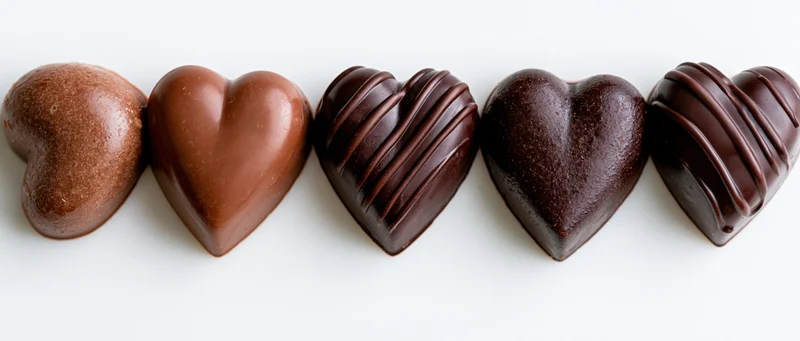 Five heart-shaped chocolate candies arranged in a row on a white background