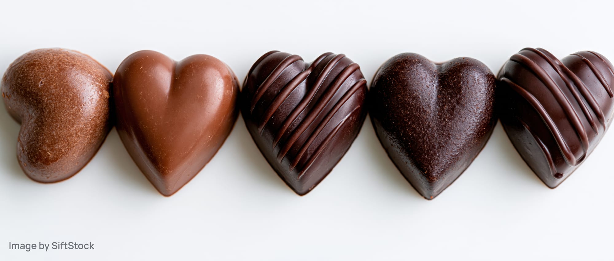 Five heart-shaped chocolate candies arranged in a row on a white background