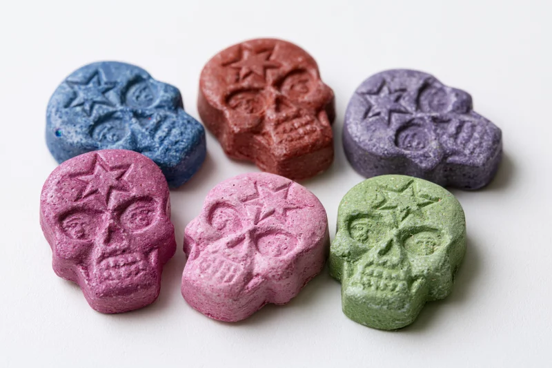 Six skull-shaped pressed tablets in various colors arranged on a white surface