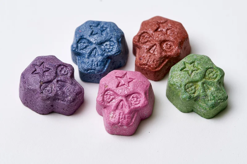 Five skull-shaped pressed tablets arranged on white surface