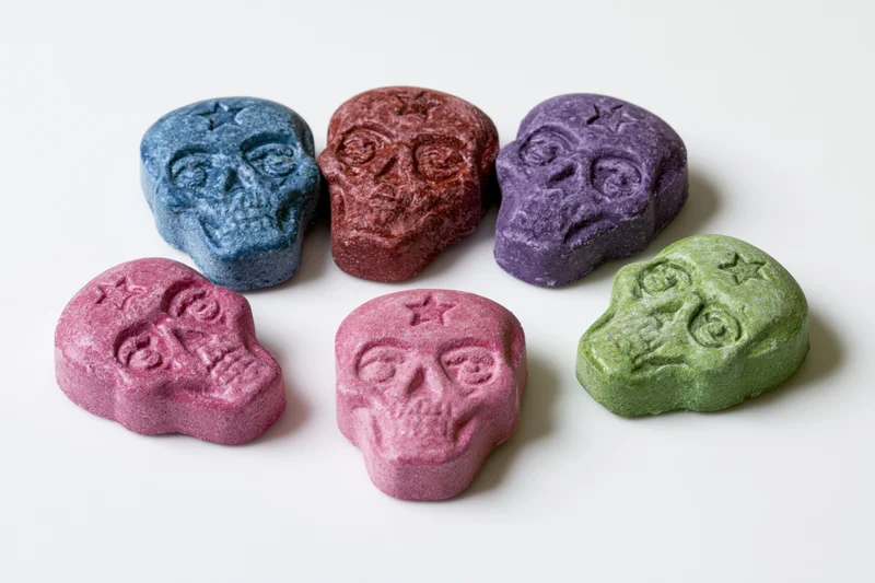 Six skull-shaped pressed candy tablets arranged on a white surface
