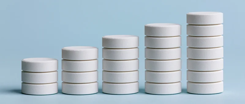Five stacks of white round pharmaceutical tablets arranged in ascending order on a light blue surface
