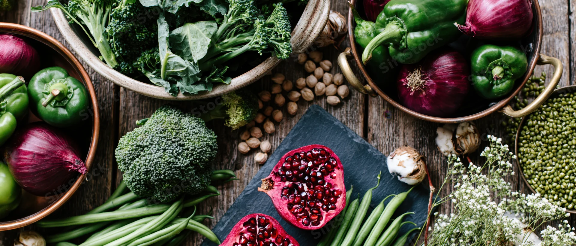 Fresh vegetables and ingredients arranged in bowls and on slate on wooden surface
