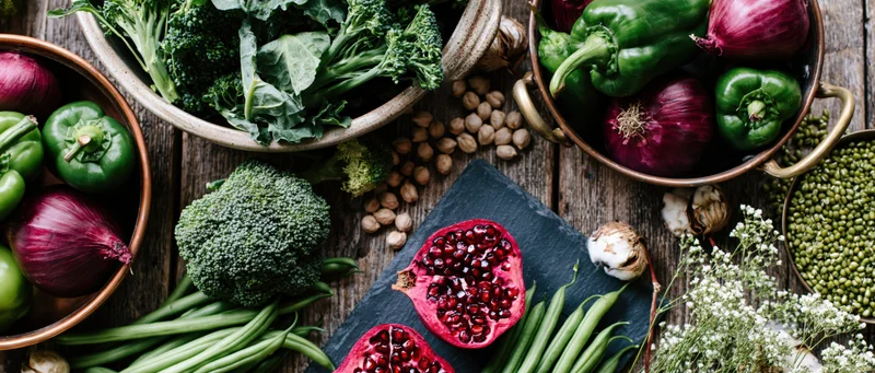 Fresh vegetables and ingredients arranged in bowls and on slate on wooden surface