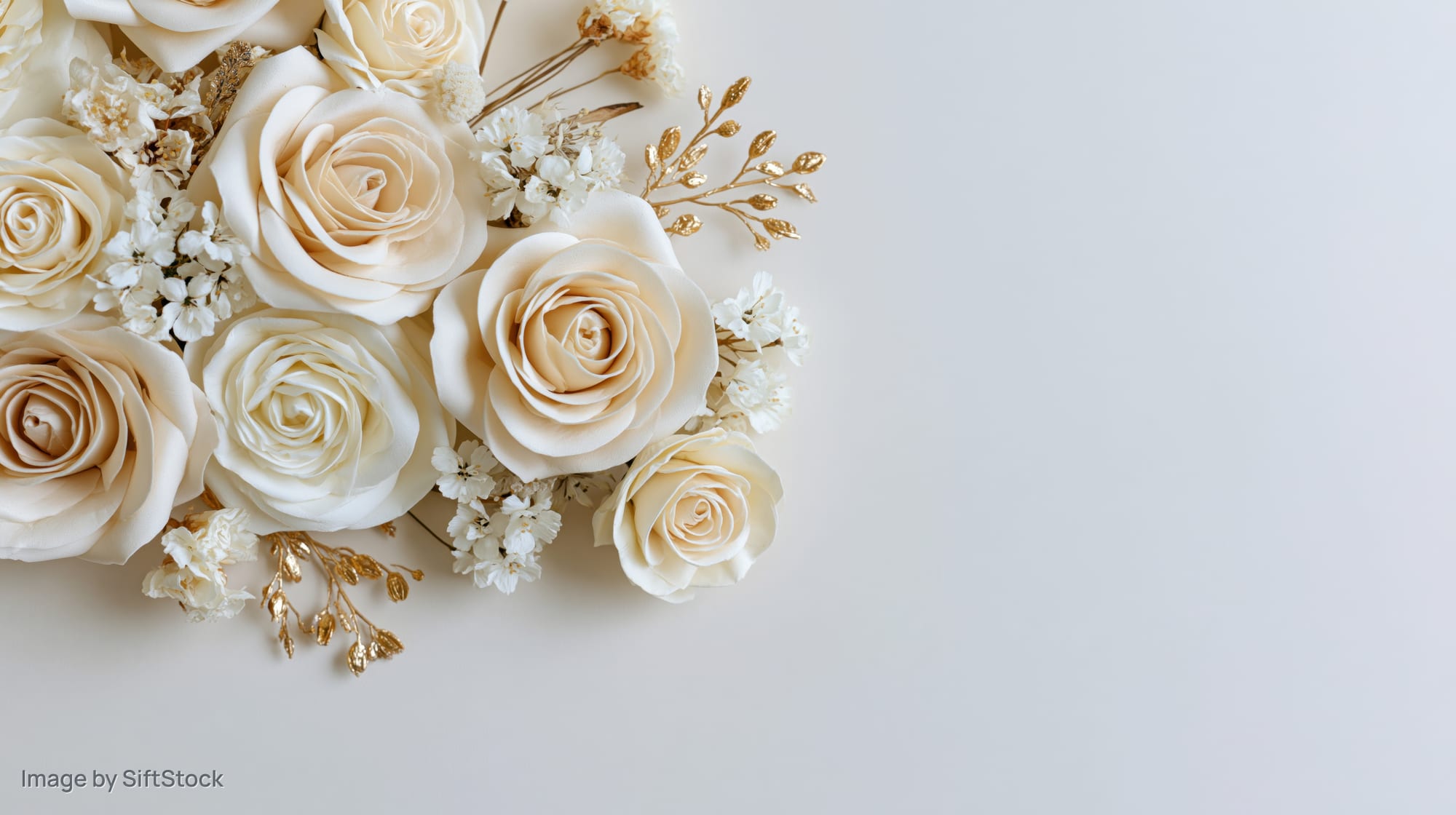 Flat lay of ivory and cream paper roses with gold foliage on white background