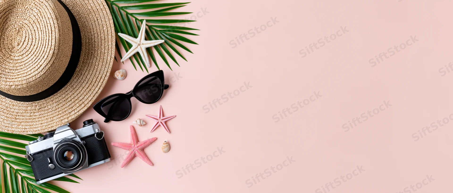 Summer travel accessories arranged with palm leaves and starfish on pink background
