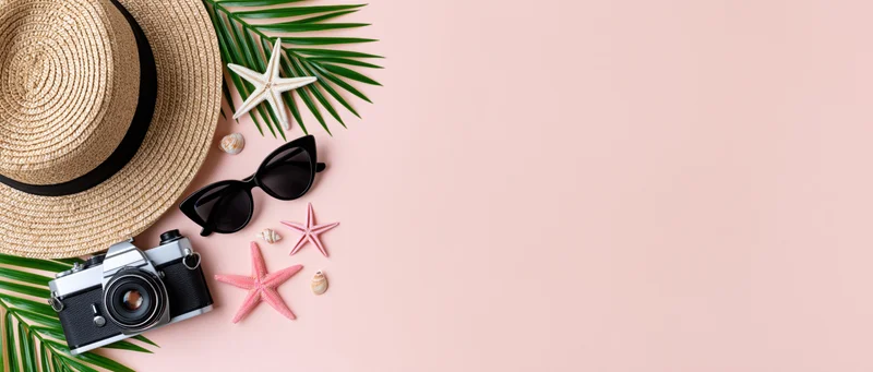 Summer travel accessories arranged with palm leaves and starfish on pink background
