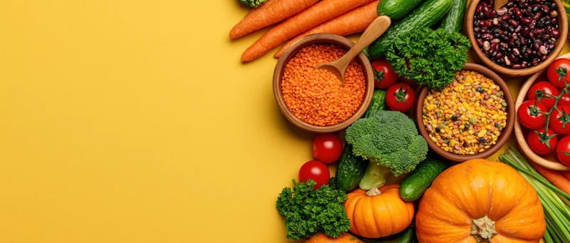 Fresh vegetables and legumes arranged in a flat lay on a yellow surface with copyspace on the left