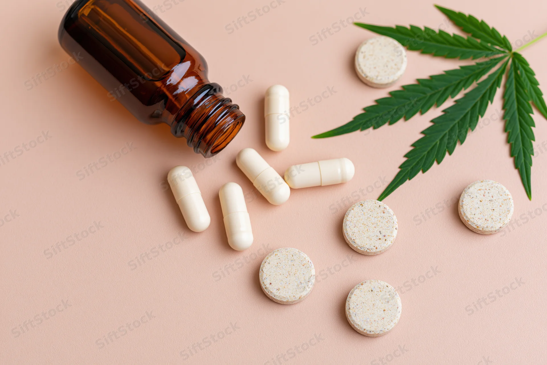 Cbd wellness products including capsules tablets and cannabis leaf arranged on pale blush background