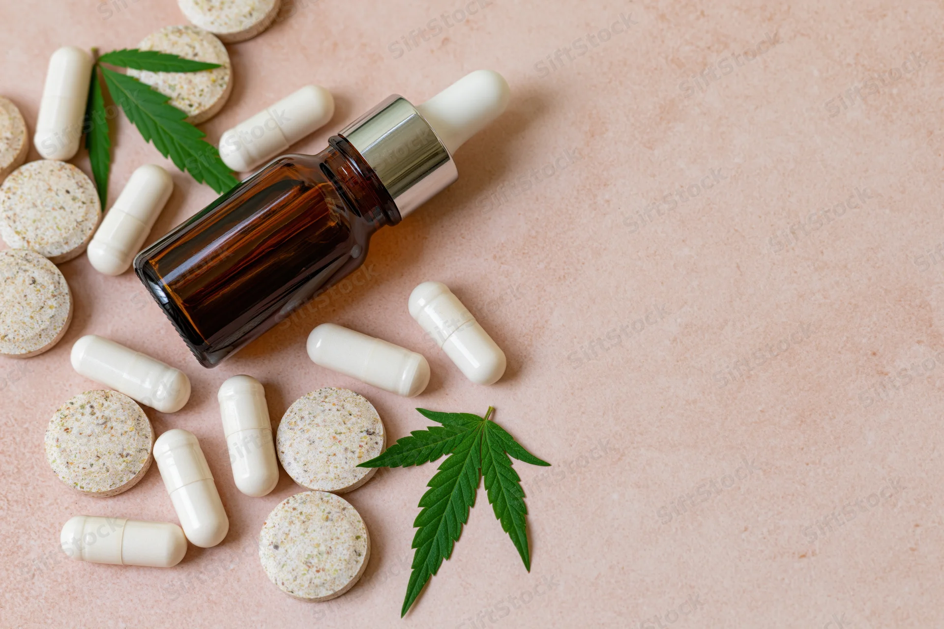 Cbd wellness products including capsules, tincture bottle and cannabis leaves arranged on blush surface