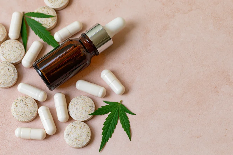 Cbd wellness products including capsules, tincture bottle and cannabis leaves arranged on blush surface