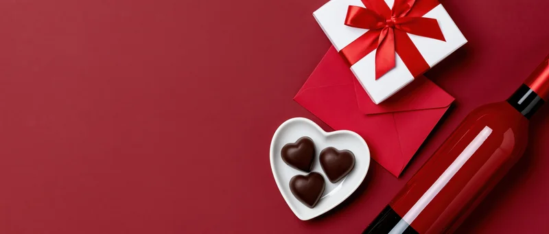 Valentines day gift arrangement with wine, chocolates, and heart-shaped box on red background