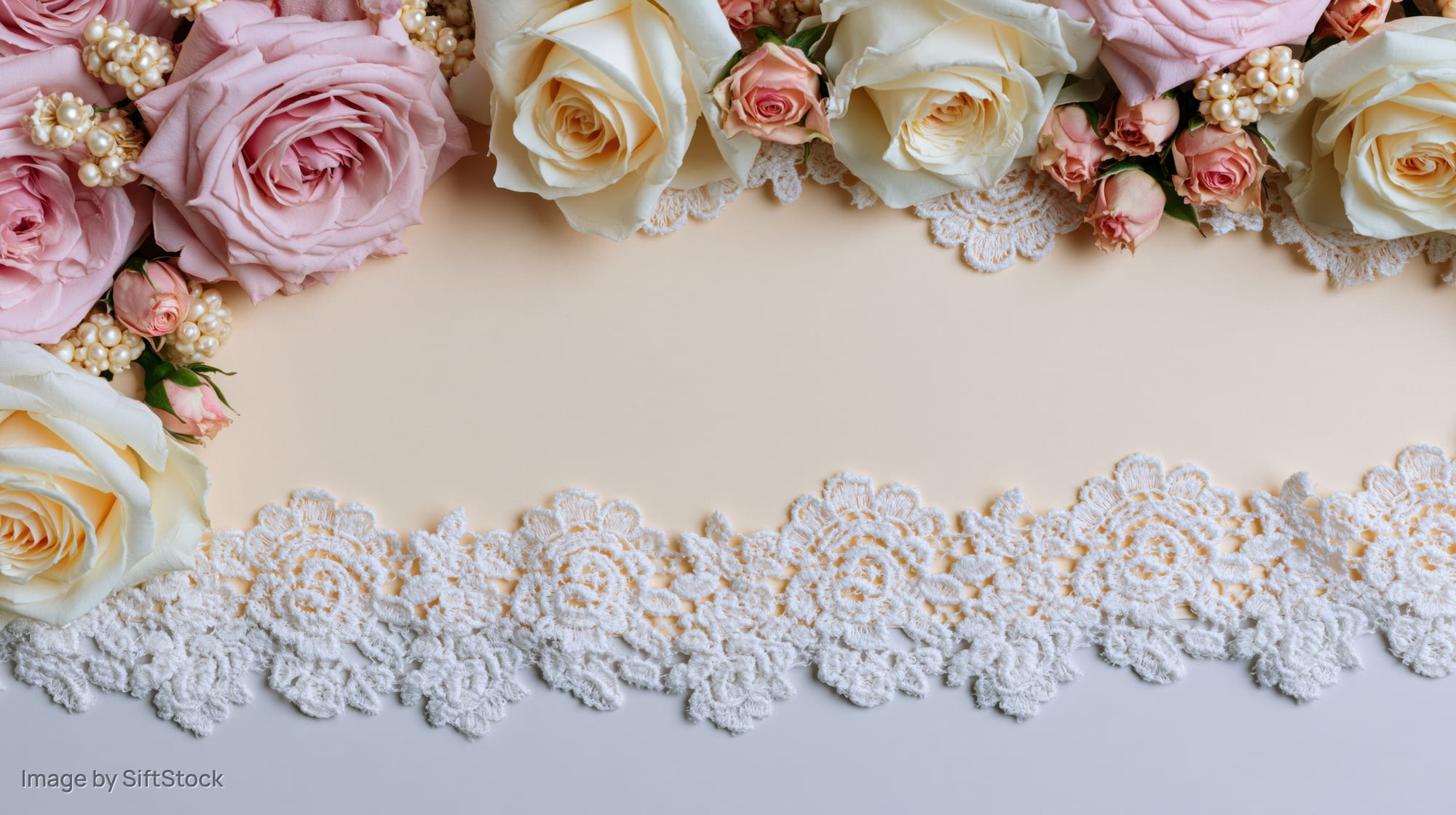 Flat lay of blush pink and cream roses with white lace trim forming a border around copyspace