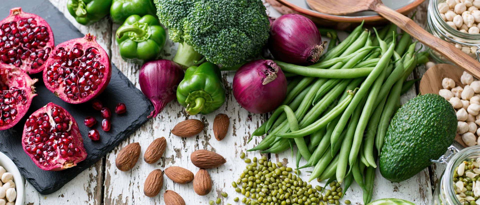 Fresh vegetables and fruits arranged with whole foods on a rustic white wooden table