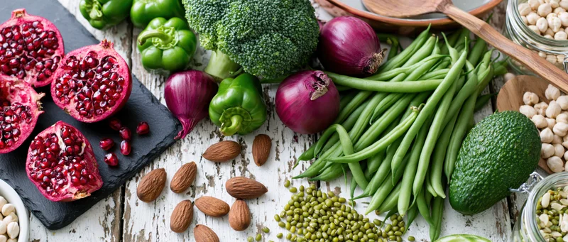 Fresh vegetables and fruits arranged with whole foods on a rustic white wooden table