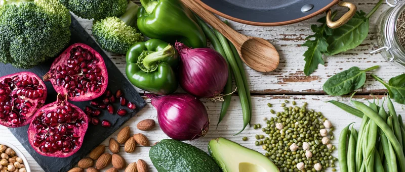 Fresh vegetables and fruits arranged with whole foods on a rustic wooden surface in a flat lay composition