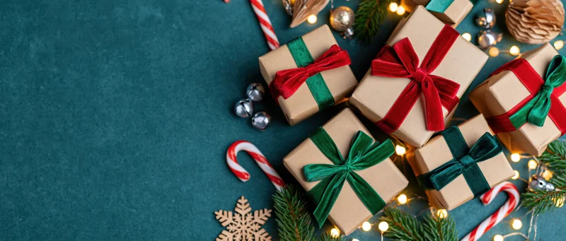 Kraft paper gift boxes with red and green velvet bows and holiday decorations on teal surface