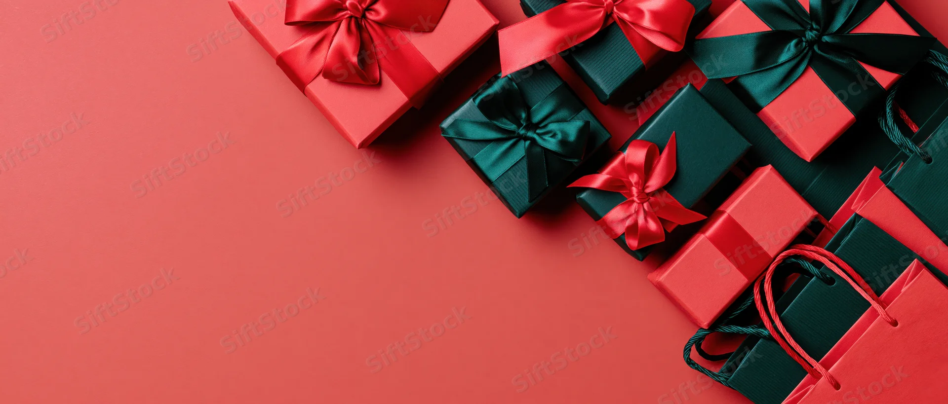 Red and dark green gift boxes with satin ribbons arranged diagonally on a red surface with copyspace
